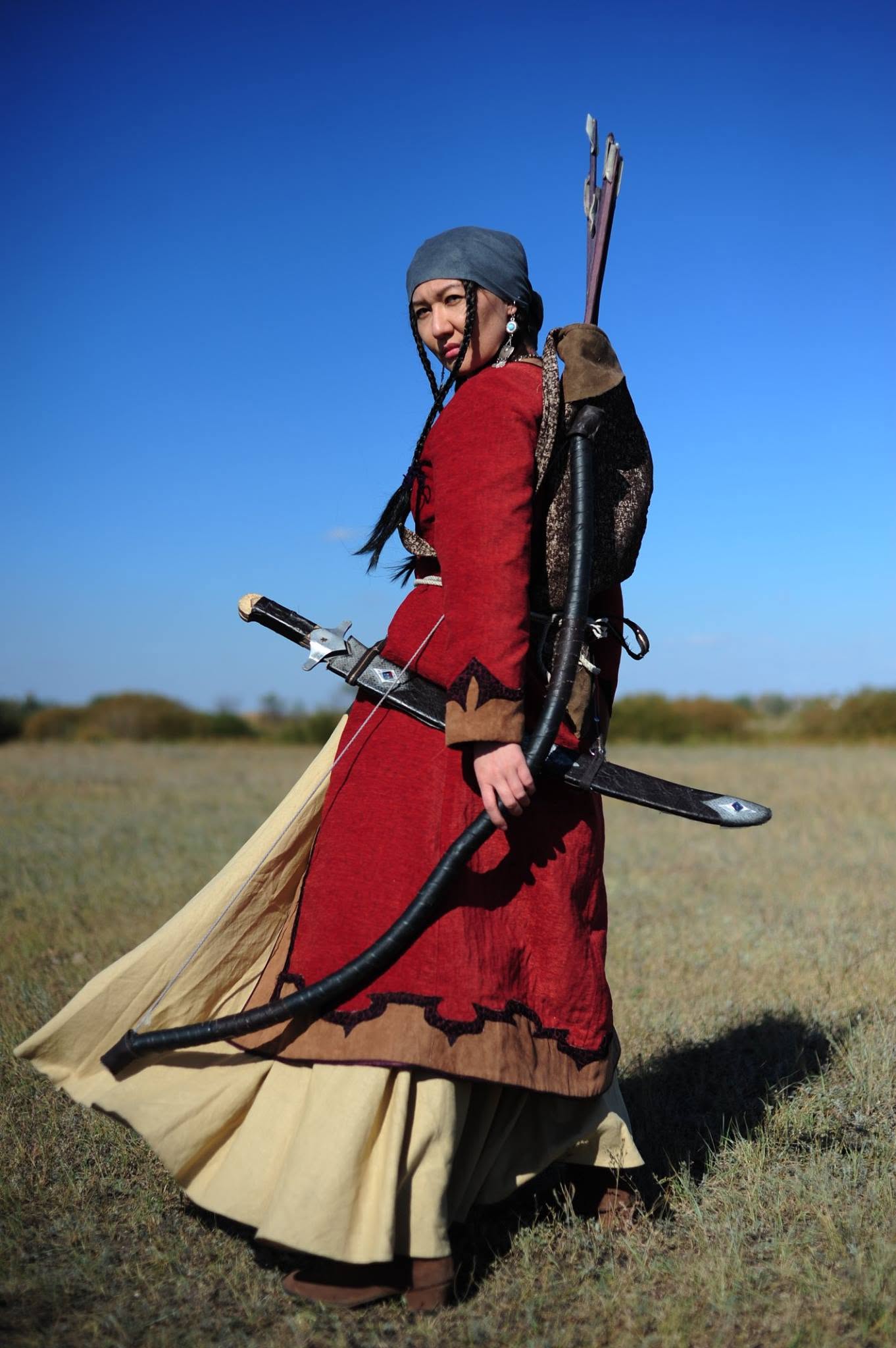Kristina Kazanjian in a red historical costume, holding a bow in the steppe